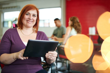Confident female designer working on a digital tablet in red creative office space