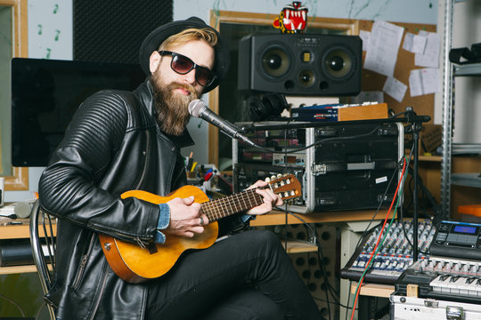 Hipster man singing and playing guitar in a studio