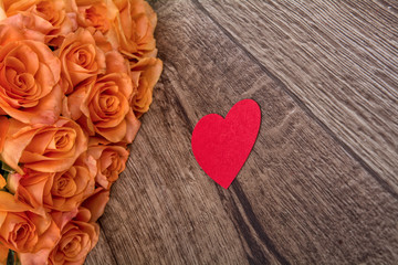 Orange roses and heart on a wooden background