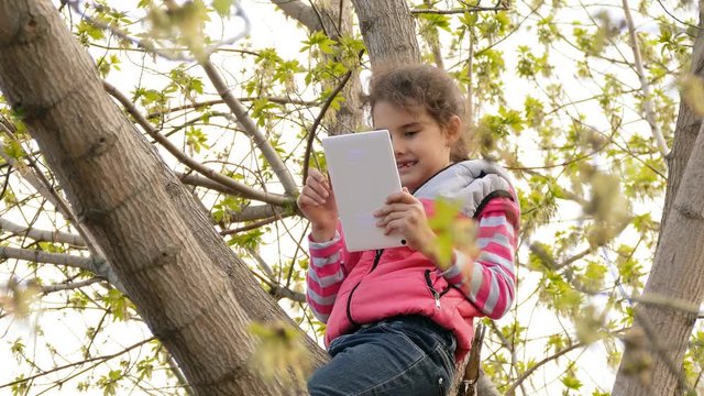 teen  girl playing tablet sitting on the tree