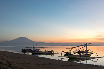 Beautiful sunrise scene at Sanur beach Bali, Indonesia. The rowboat or “Jukung” is widely used as fishing boat by the local fisherman. Mount Agung is distant background.