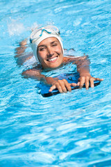 femme souriante pratiquant la natation dans une piscine avec une planche et un masque