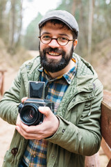 Obraz premium Young man bearded with film photocamera in the forest