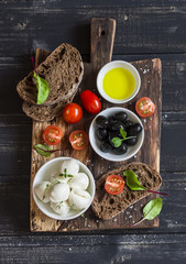 Mediterranean snack - mozzarella, olives, rye ciabatta bread, cherry tomatoes on a rustic wooden cutting board