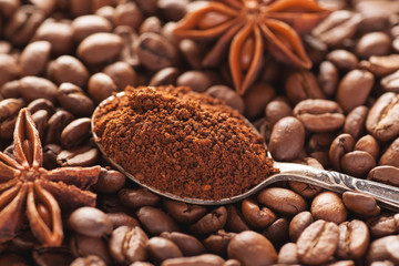 Grounded coffee in silver spoon above coffe beans