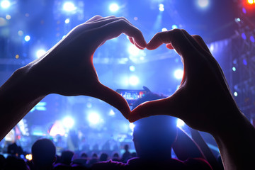 Silhouette of a heart shaped hands and crowd of Audience at live concert, light illuminated is power of music concert