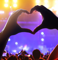 Silhouette of a heart shaped hands and crowd of Audience at live concert, light illuminated is...