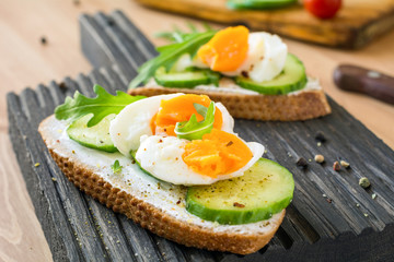 Healthy toast with cucumber, arugula and egg on wooden cutting board, close up view