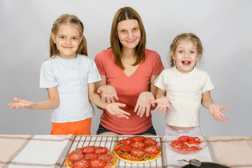 Obraz na płótnie Canvas Mom with two young daughters happily show made pizza with tomatoes