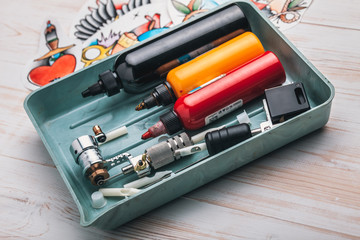 Replacement supplies for tattoo in sterile packages, sketches, inks and a tattoo machine on the white background of old boards