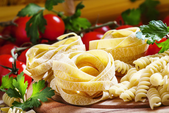 Assorted dry pasta, cherry tomatoes and parsley on a vintage woo