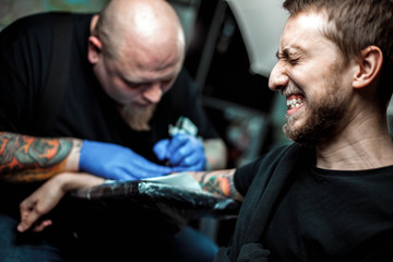 master tattooist makes a tattoo on the skin. The client narrows his eyes and turns away, the...