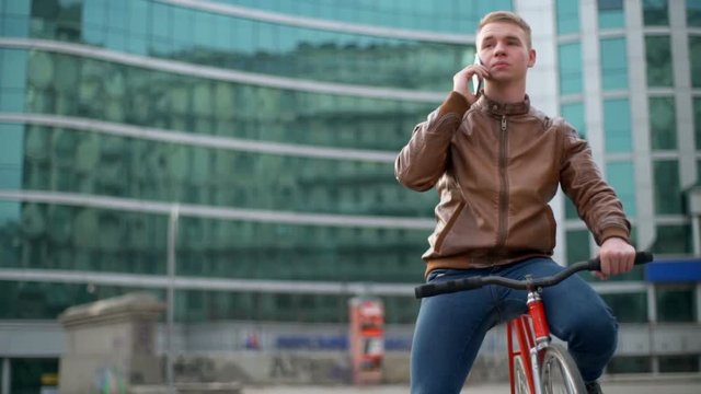 young male bicyclist talks on the phone in downtown slow motion