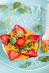 Mango rice pudding with fresh strawberries on a blue plate and a wooden spoon.