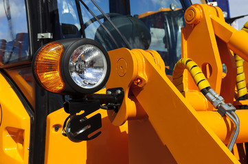 Bulldozer headlight, huge orange powerful construction machine with light equipment also used for tractors, excavators, loaders and other machines, focused on spotlight, selective focus 