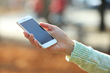 A female hand holding a mobile phone outdoors, on blurred background
