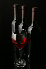 Red wine glass against bottles in a row on black background, close up