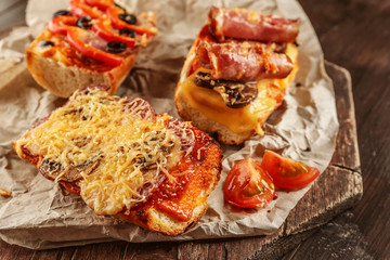 Hot pizza baguettes with bacon, salami and cheese on wooden table