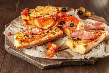 Hot pizza baguettes with bacon, ham, salami and olives on wooden table