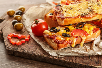 Hot pizza baguettes with olives, salami and cheese on wooden table
