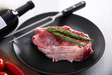 Raw pork steak with meat fork and rosemary on black plate