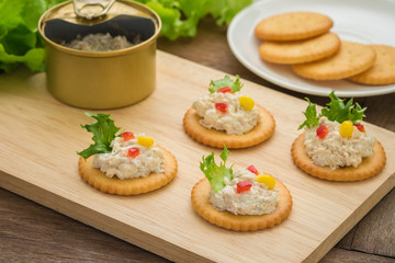 Crackers with tuna salad on wooden plate and tuna spread in canned