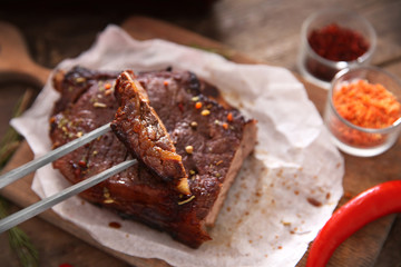 Sliced roasted pork steak with meat fork and spices on wooden background