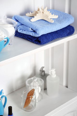 Bathroom set with towels, starfish and sponges on a shelf in light interior