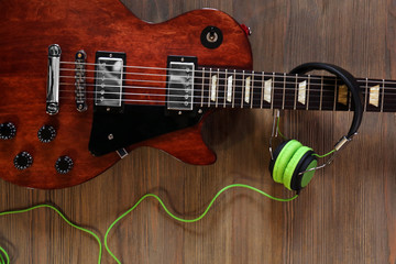 Fototapeta premium Brown electric guitar with headphones on wooden background