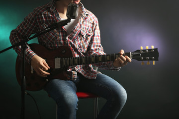 Young man playing electric guitar with microphone on lighted dark background