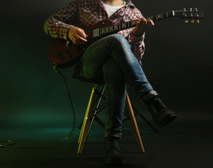 Young man playing electric guitar on lighted dark background