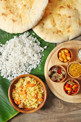 Boiled and fried rice with vegetables, flat bread on banana leaf over wooden background