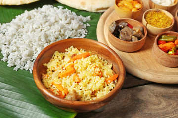 Boiled and fried rice with vegetables on banana leaf over wooden background