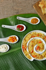 Fried rice with flat bread and spices on banana leaf over wooden background