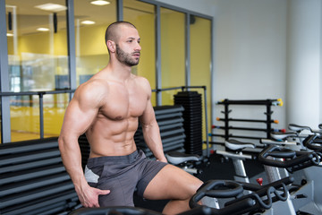 Muscular Man Doing Cycling In Modern Fitness Center