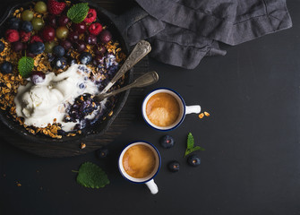 Healthy breakfast. Oat granola crumble with fresh berries, seeds and ice-cream in iron skillet pan on dark wooden board over black backdrop