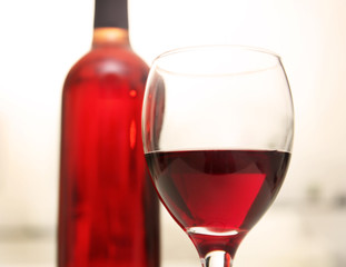 Glass of red wine with bottle on blurred interior background