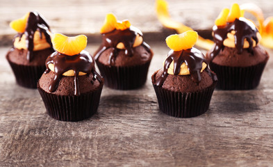 Tasty cupcakes with slice of mandarin and chocolate on wooden background