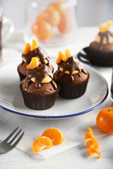 Three tasty cupcakes with slice of mandarin and chocolate on a plate over light wooden background