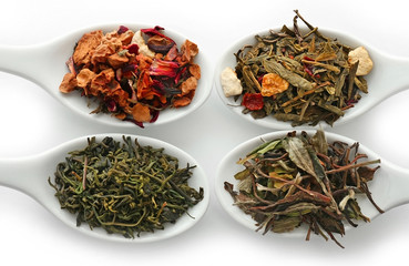 Different sorts of dry tea in ceramic spoons, isolated on white