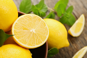 Fresh lemons with green leaves in bowl closeup