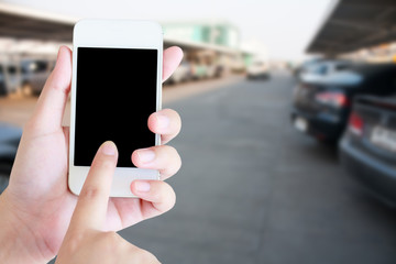 hand holding mobile phone with blur car park