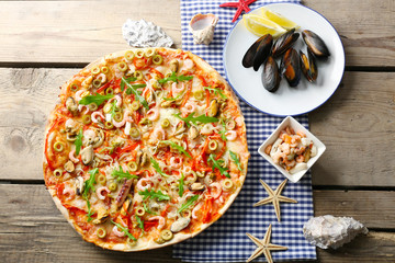 Pizza with seafood, red pepper and green olives on wooden table