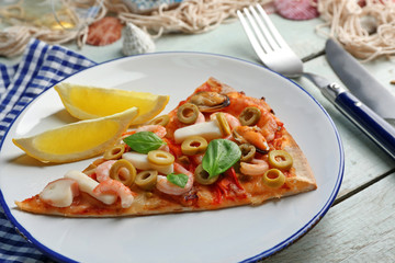 Pizza slices with seafood, red pepper and green olives on wooden table