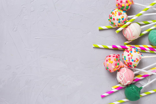 Colorful cake pops and paper straws on  grey textured  backgroun