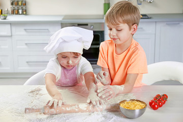 Two little boys rolling out a pizza dough, close up