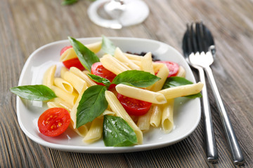 Plate of pasta with cherry tomatoes and basil leaves on table closeup