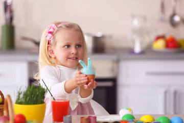 Little girl holding Easter egg with knitted hat in the kitchen