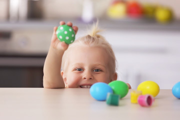 Little girl at the wooden table with painted Easter eggs in the kitchen