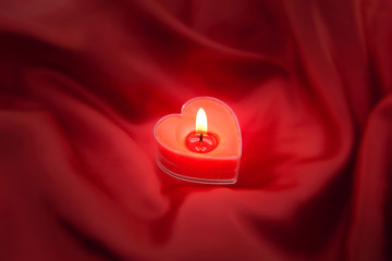 Red burning heart shaped candle on satin background. 